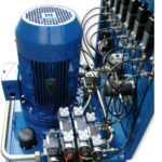 Blau lackiertes Hydraulikaggregat mit großem Elektromotor, mehreren Hydraulikventilen, Leitungen und Verschraubungen.