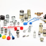 Verschiedene Hydraulikkupplungen, Steckverbinder, Verschraubungen und Schutzkappen in mehreren Größen und Farben liegen sortiert auf weißem Hintergrund.
