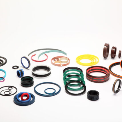 Bunte Hydraulikdichtungen, Führungsringe und O-Ringe in unterschiedlichen Größen und Materialien sind auf weißem Hintergrund ausgebreitet.