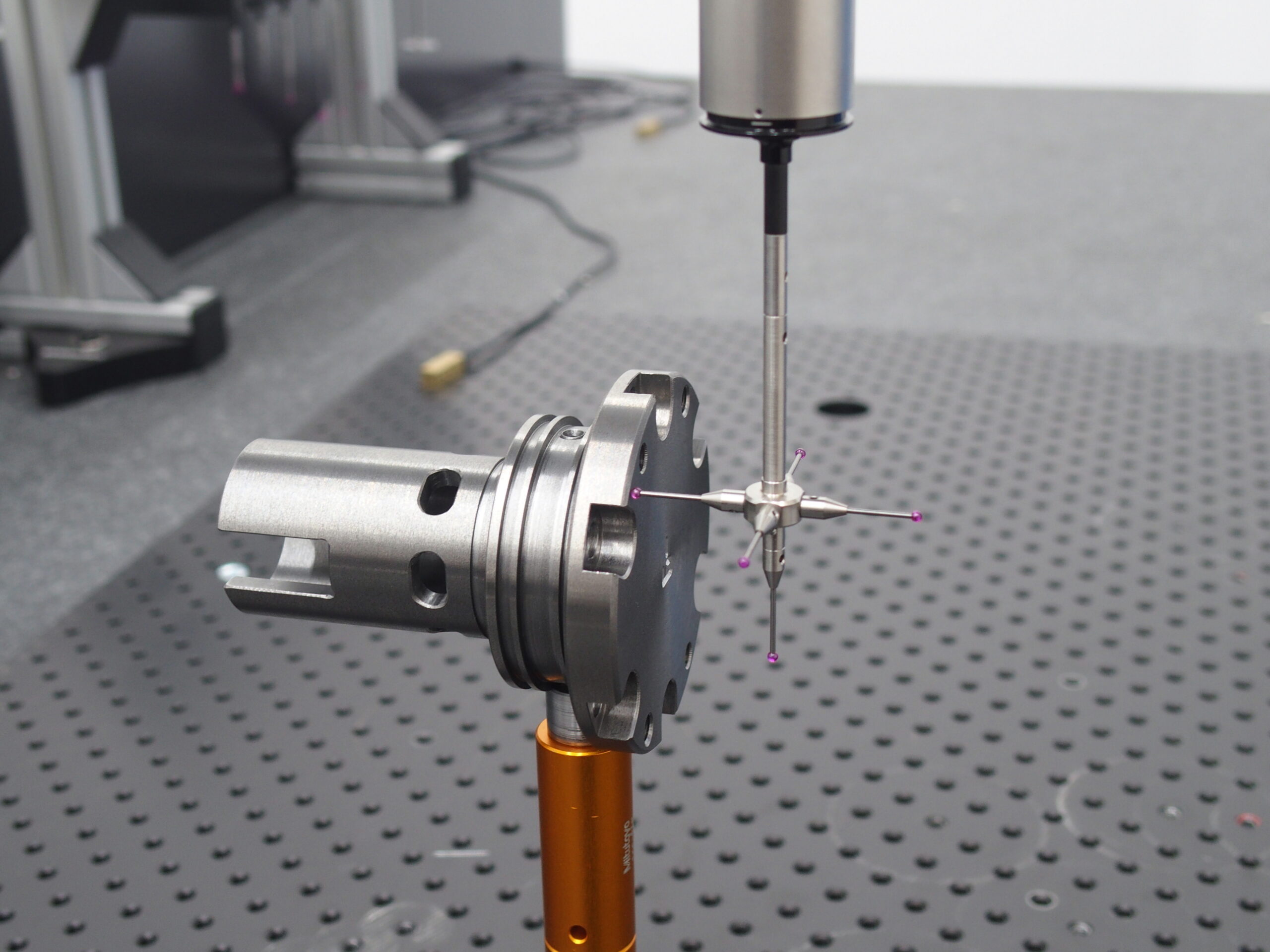 Ein Koordinatenmessgerät mit taktilem Mehrfach-Messkopf prüft ein metallisches Präzisionsbauteil, das auf einem Halter fixiert ist. Die Messstifte mit violetten Tastkugeln berühren das Werkstück, um Form- und Maßgenauigkeit zu erfassen.