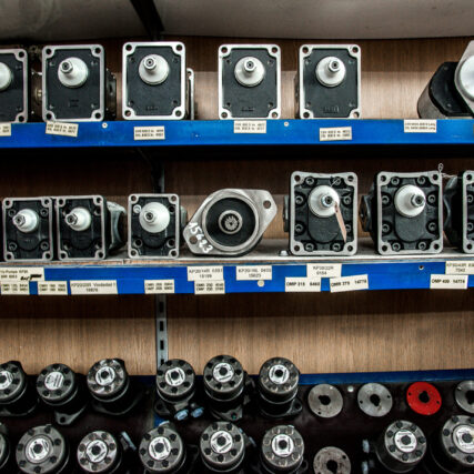 Verschiedene Hydraulikpumpen und Motoreinheiten stehen geordnet in einem blauen Metallregal mit beschrifteten Ablagefächern.