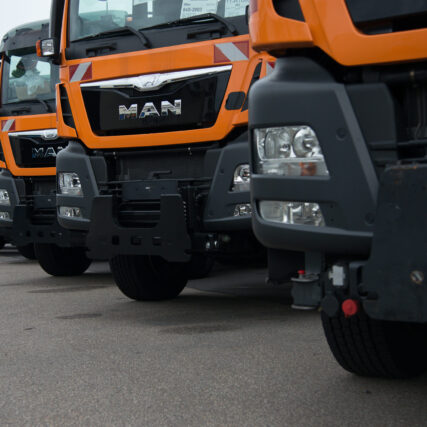 Nahaufnahme der Frontbereiche mehrerer MAN-LKW in Winterdienst-Ausführung, mit typischer orangefarbener Lackierung und robusten Anbausystemen.